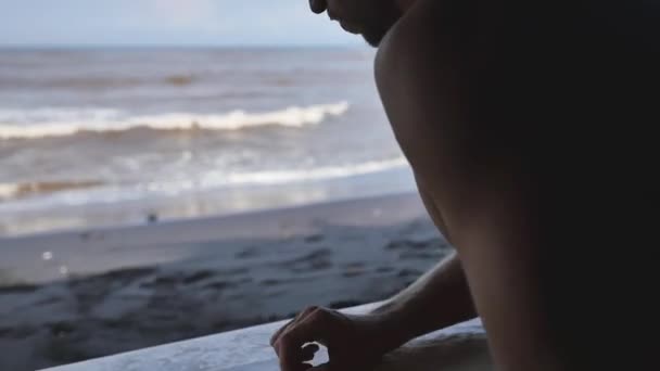 Surfista se sienta en la cueva y encerando su tabla de surf. Bali. . — Vídeo de stock