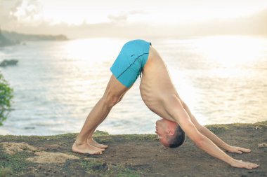Cliff mavi deniz arka plan ile Yoga yapan yakışıklı erkek