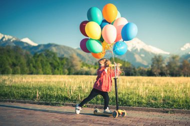 Çocuklar güneşli yaz gününde bir parkta scooter binmek öğrenirler. Okul öncesi çocuk ve bir rulo sürme güvenlik kask kız. Çocuklar açık havada scooter ile oynamak. Etkin boş ve çocuk için açık spor.