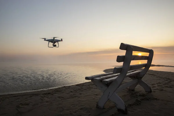 Güneşin doğuşunda bir dron ve ahşap bir bank üzerinde uçar..