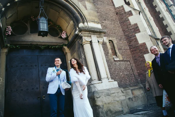 Noiva e noivo jogam o arroz na frente da velha porta gótica — Fotografia de Stock