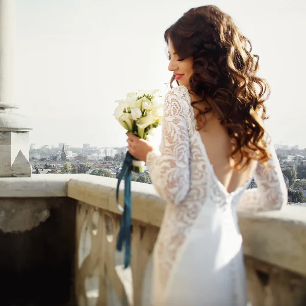 Bride poses back with lily bouquet with cityscape on the background — Stock Photo, Image