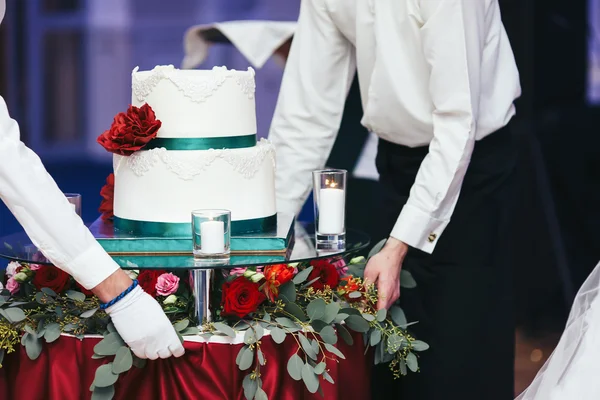 Pincér hozza egy fehér esküvői torta díszített asztalon — Stock Fotó