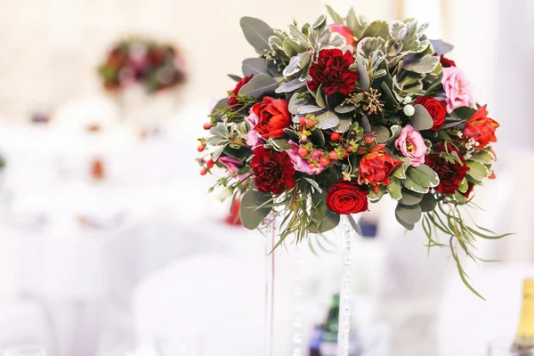 Red bouquet of greenery and roses on the high vase