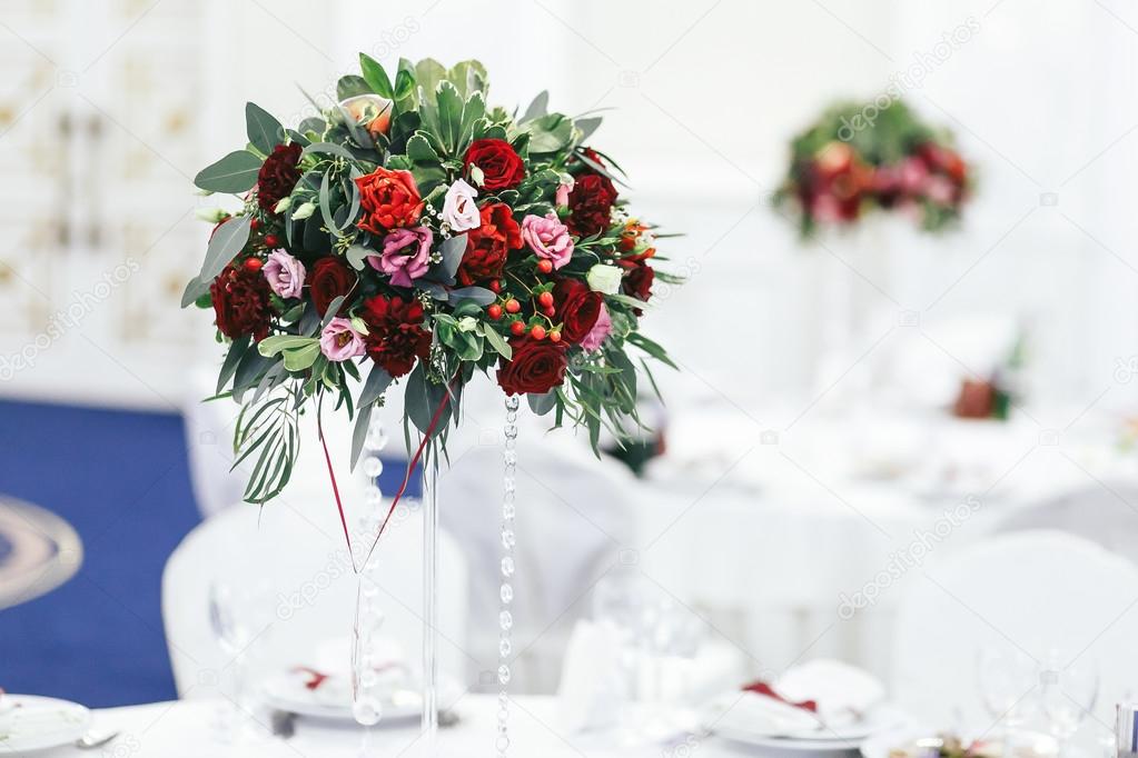 Red bouquet of greenery and roses on the high vase on the weddin