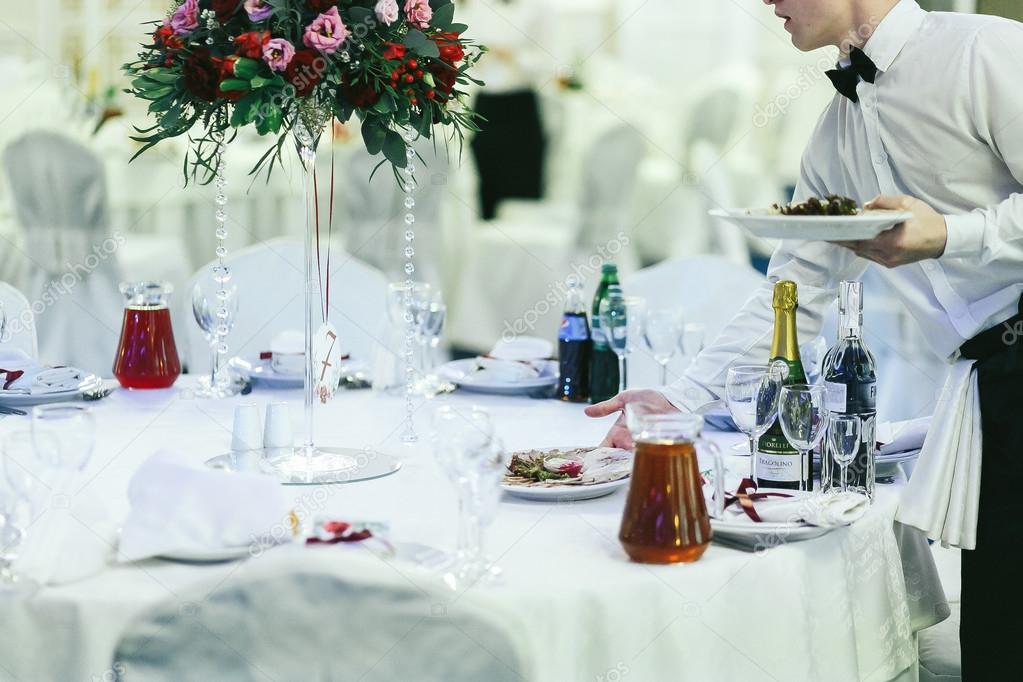 Waiter puts dishes on the white table 