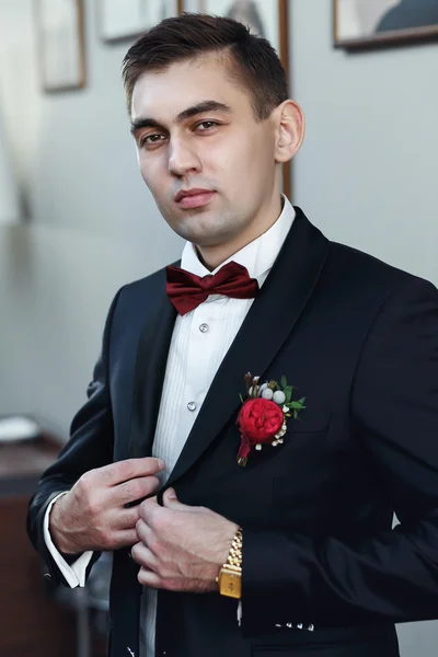 Confident young man in tuxedo with bow tie posing at camera  hol — Stock Photo, Image