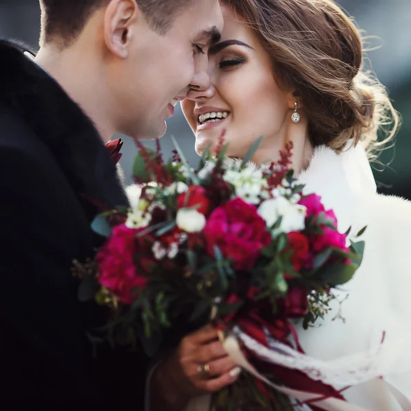 Newlyweds touch each other with noses, while bride holds a bouqu — Stock Photo, Image