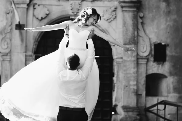 Groom levanta uma noiva enquanto está em pé na frente de um castelo — Fotografia de Stock