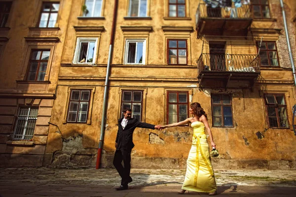 Sposo tiene la mano della sposa e la tira lungo una vecchia casa — Foto Stock