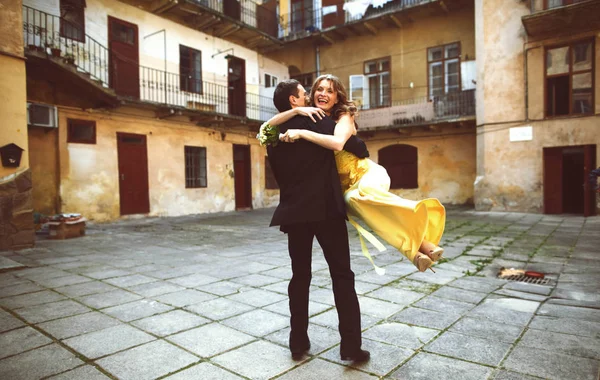 Bräutigam wirbelt Braut im gelben Kleid im Hof — Stockfoto