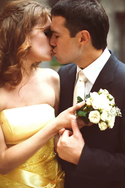 Bruidegom kussen een bruid terwijl ze een boeket witte rozen houdt — Stockfoto