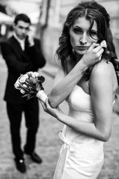 Νύφη φαίνεται κουρασμένος εκμετάλλευση τριαντάφυλλα στα χέρια της, ενώ γαμπρός συνομιλίες o — Φωτογραφία Αρχείου