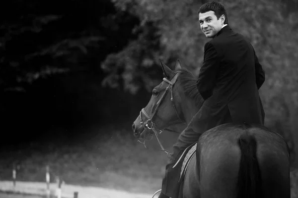 Ο άνθρωπος σε μαύρο κοστούμι στροφές ενώ οδηγά ένα άλογο — Φωτογραφία Αρχείου