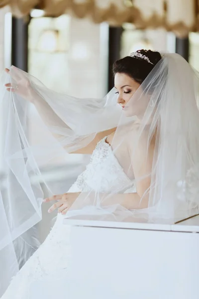 Bride\'s face is hidden behind a veil while she stands leaned on