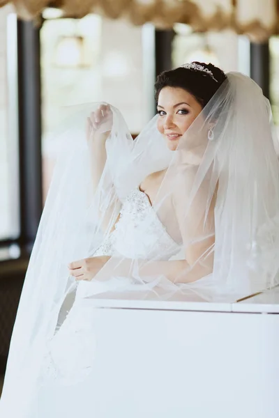 Невеста улыбается над завесой, когда она стоит, опираясь на пианино — стоковое фото