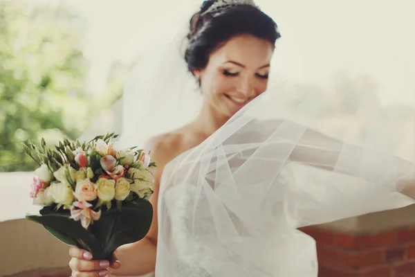 Mariée sourit derrière un voile tenant un bouquet de mariage dans son bras — Photo