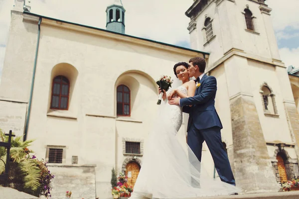 Ženich líbá nevěstu přední bílé katedrála — Stock fotografie