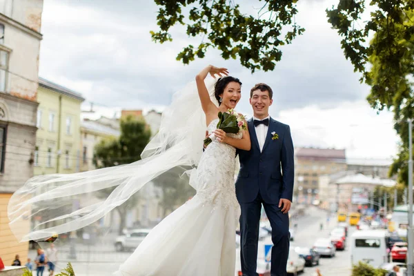 Braut und Bräutigam lächeln und posieren vor einem großartigen Stadtbild — Stockfoto
