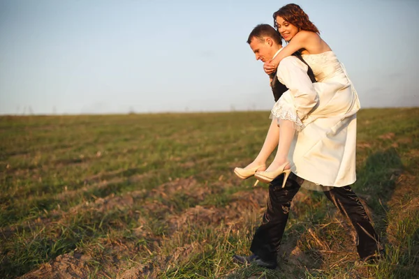 Novio lleva novia a través del campo — Foto de Stock