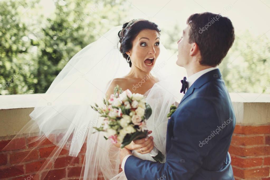 Funny bride looks shocked being hugged by a groom