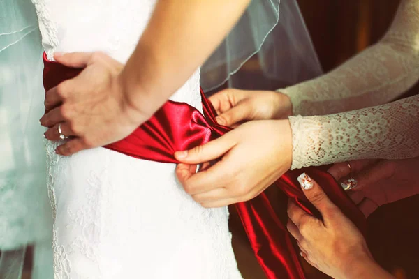 Le mani delle donne regolano una cintura di raso rosso sulla vita della sposa — Foto Stock