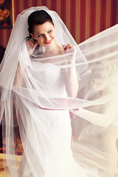 Мечтательная невеста улыбается, пока подружка невесты настраивает свое платье — стоковое фото