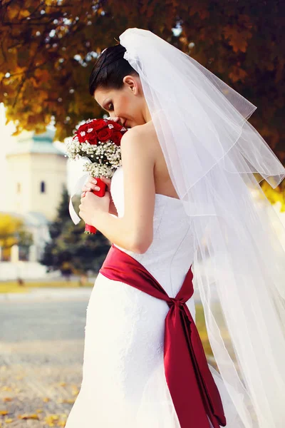 Delicado novia con un cinturón rojo en su dresss huele un bo de boda —  Fotos de Stock