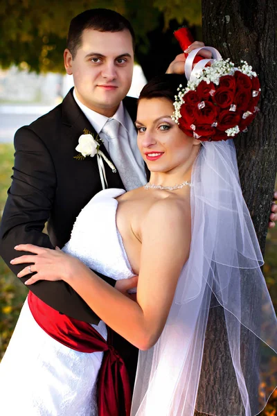 Noiva mantém um buquê de casamento sob uma cabeça, enquanto o noivo a abraça — Fotografia de Stock