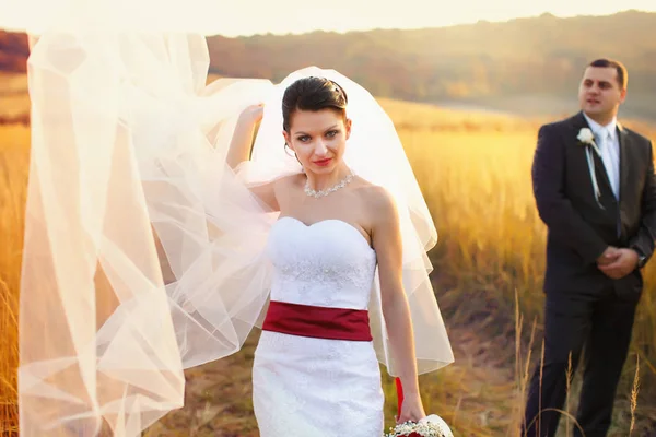 Sposa fiduciosa attraverso un velo sul vento mentre lo sposo sta in piedi — Foto Stock