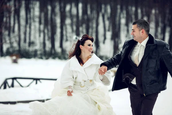 Нареченій і нареченій весело бігають по парку в снігопаді — стокове фото