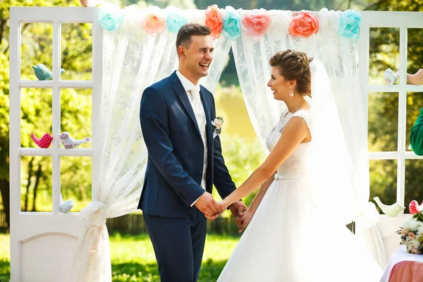 Bräute halten Händchen in der Nähe des Hochzeitsbogens — Stockfoto