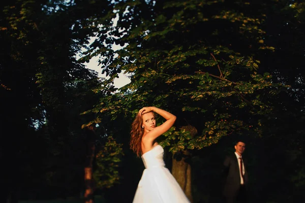 Mariée mélange ses cheveux debout dans les lumières du coucher du soleil dans le par — Photo