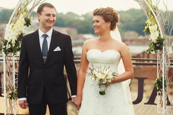 Bruidegom kijkt met liefde een prachtige bruid permanent onder een alta — Stockfoto