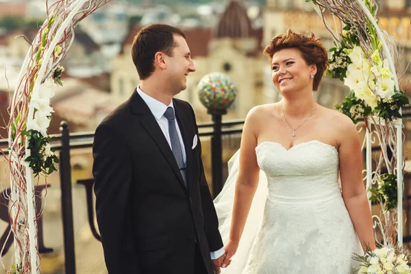 Nowożeńcy uśmiech, patrząc na siebie i stnading na dachu — Zdjęcie stockowe