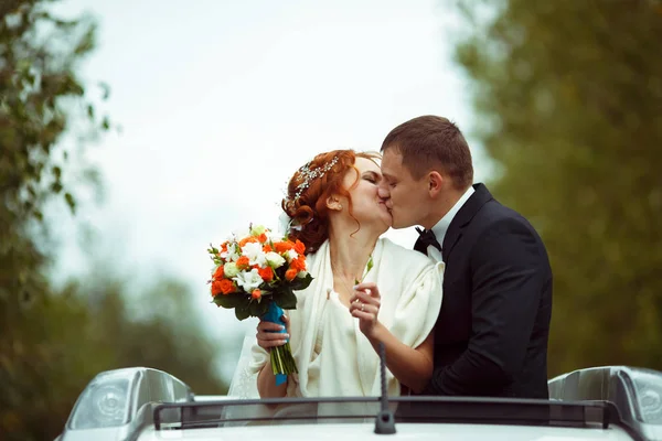 Счастливые молодожёны целуются, стоя в люке машины — стоковое фото