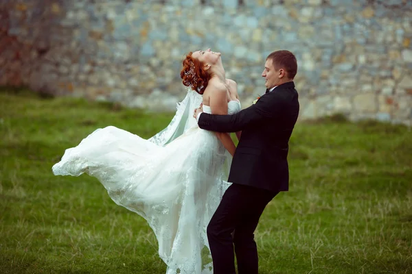 Γαμπρός περιστρέφει μια εντυπωσιακή νύφη που στέκεται πάνω σε πράσινη χλόη — Φωτογραφία Αρχείου