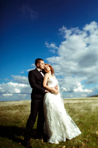 Sposo abbraccia una sposa da dietro in piedi sotto i raggi del sole sul fi — Foto Stock