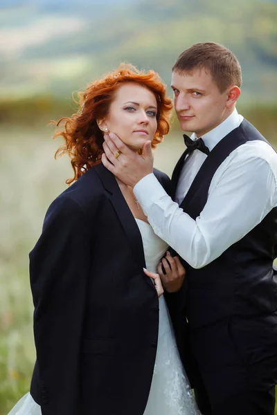 Handsome groom holds bride chin tenderly while she wears his jac — Stock Photo, Image