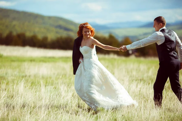 Noiva no casaco do noivo corre através do campo segurando sua mão — Fotografia de Stock