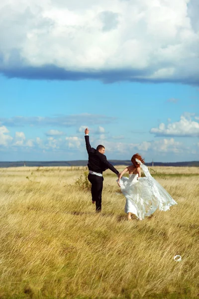 Sposa e sposo camminano saltando lungo il campo con un tempo splendente — Foto Stock