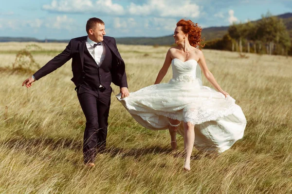 Novia y novio se ven divertidos caminando en el campo en un vertedero ventoso — Foto de Stock