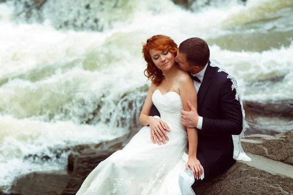 Groom beija o pescoço de uma noiva de pé atrás de uma montanha — Fotografia de Stock