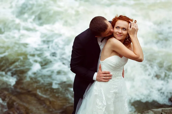 Sposo bacia una sposa abbracciandola da dietro, in piedi nel fr — Foto Stock