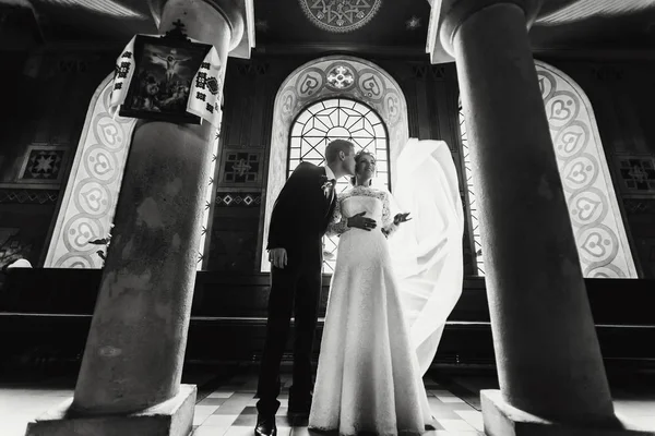 Groom embrasse la joue de la mariée posant dans le hall de l'église — Photo