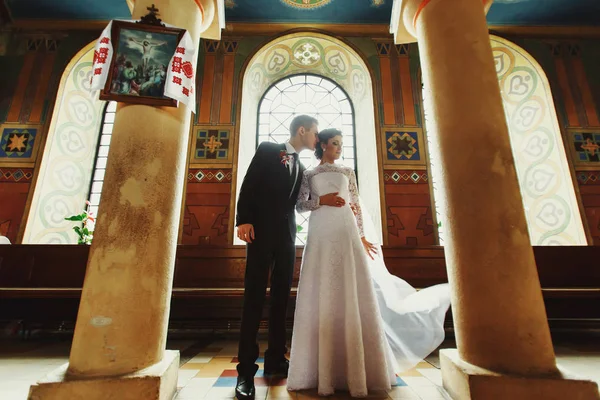 Γαμπρός αγγίζει νύφη ευγενικά στέκεται μεταξύ των πυλώνων σε c — Φωτογραφία Αρχείου