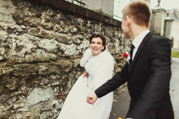 Sposo tiene la mano della sposa mentre corrono lungo la strada — Foto Stock