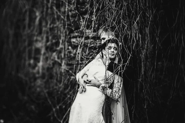 En bröllopsparet kramar ömt står bakom torra grenar av i — Stockfoto