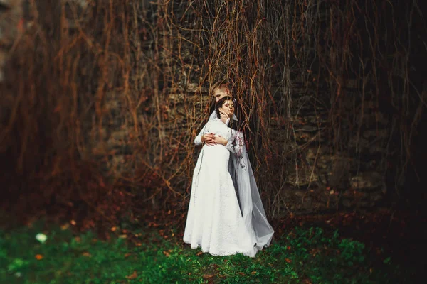 Bruid staat achter een bruidegom onder een droge ivy vertakkingen — Stockfoto