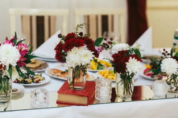 Red and white chrisantames stand in glass vases on books — Stock Photo, Image